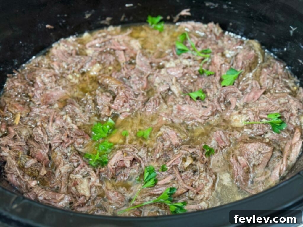 Deliciously cooked shredded beef, garnished with fresh parsley, simmering in its own rich juices within the slow cooker. Ready to be served.