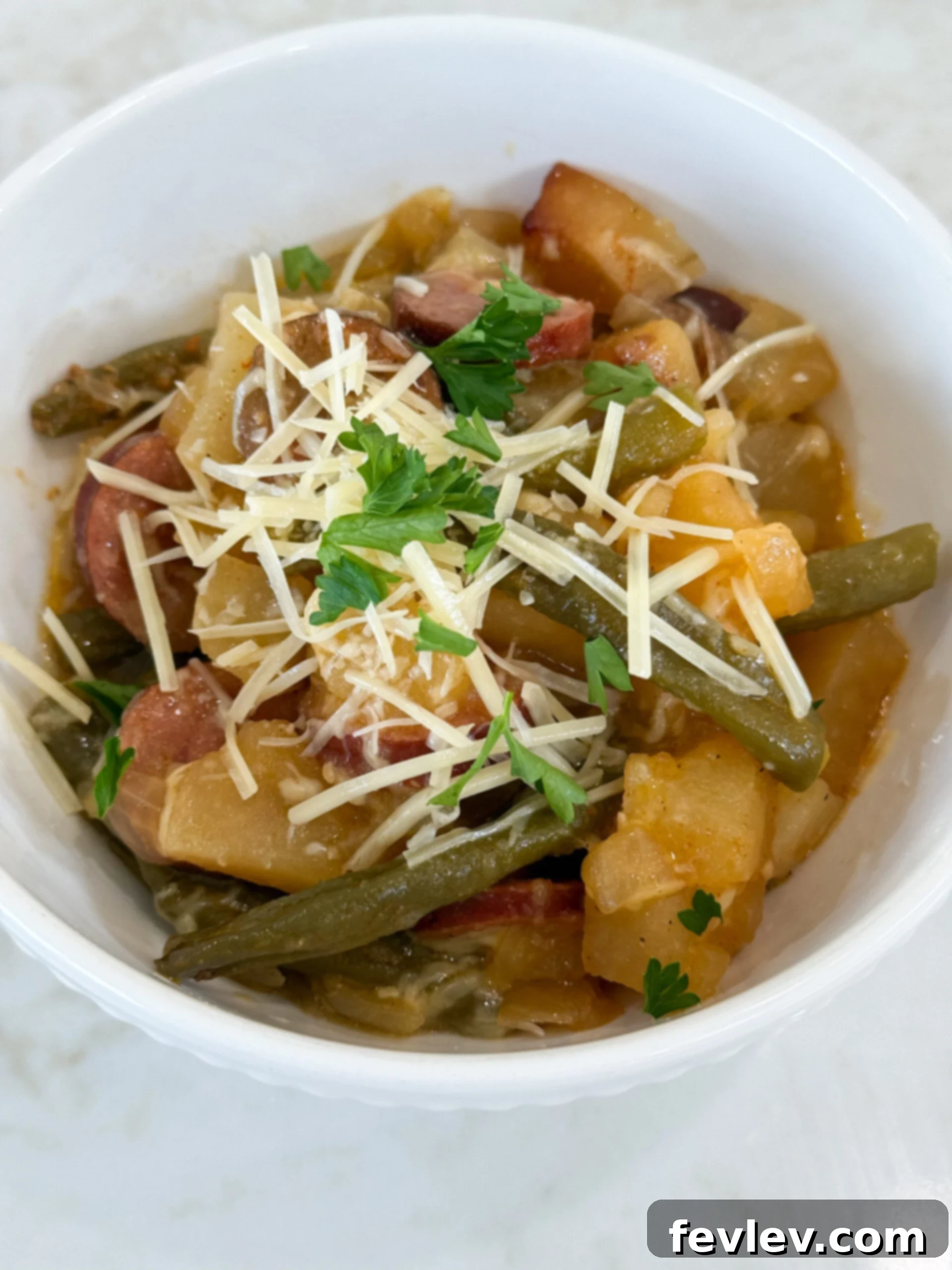 Hearty Slow Cooker Kielbasa with Potatoes and Green Beans 2 Cooked sausage, potatoes, and beans in a white bowl topped with Parmesan cheese and fresh parsley