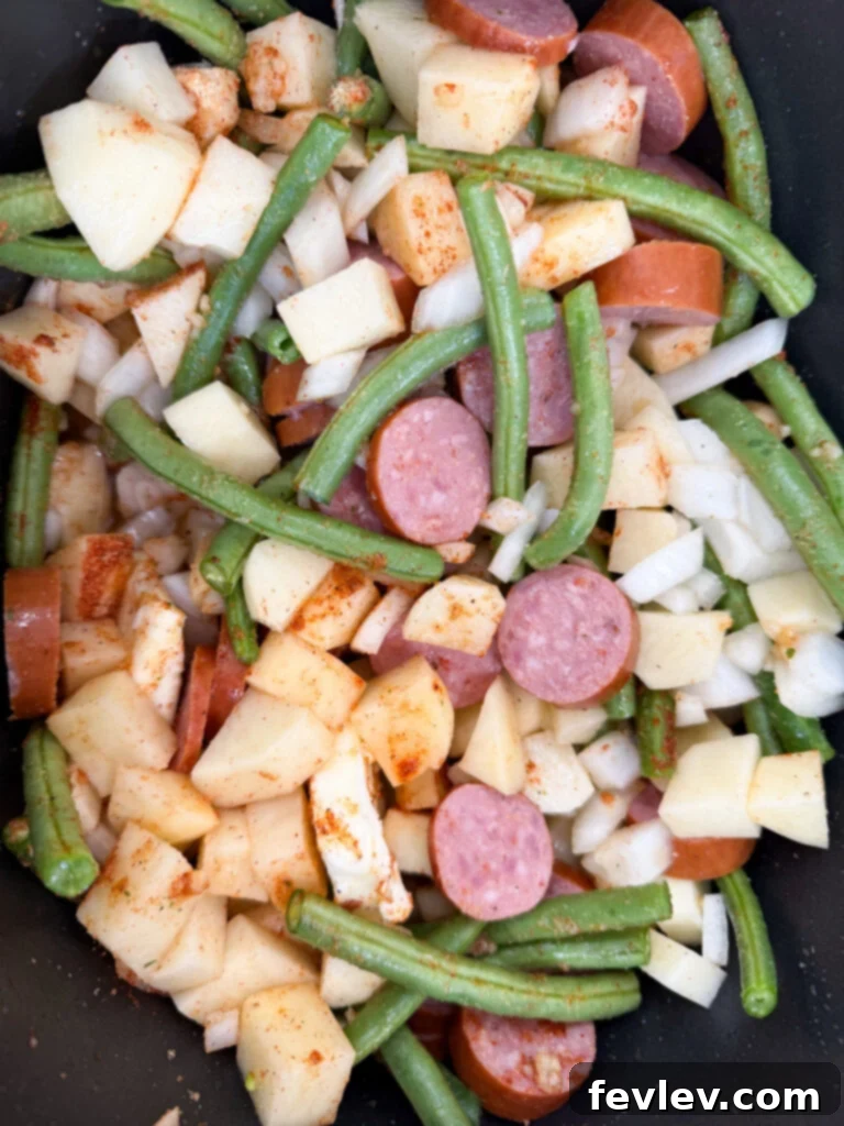 Hearty Slow Cooker Kielbasa with Potatoes and Green Beans 7 Prepared sausage, green beans, diced onions and potatoes in a slow cooker, topped with butter slices, ready to cook.