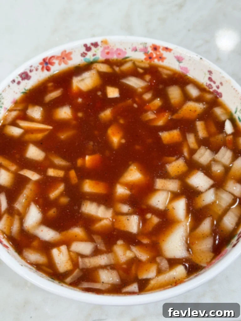 Diced yellow onions soaking in a rich, dark Hawaiian BBQ sauce in a white bowl, garnished with a pink flower, suggesting a blend of savory and tropical flavors.