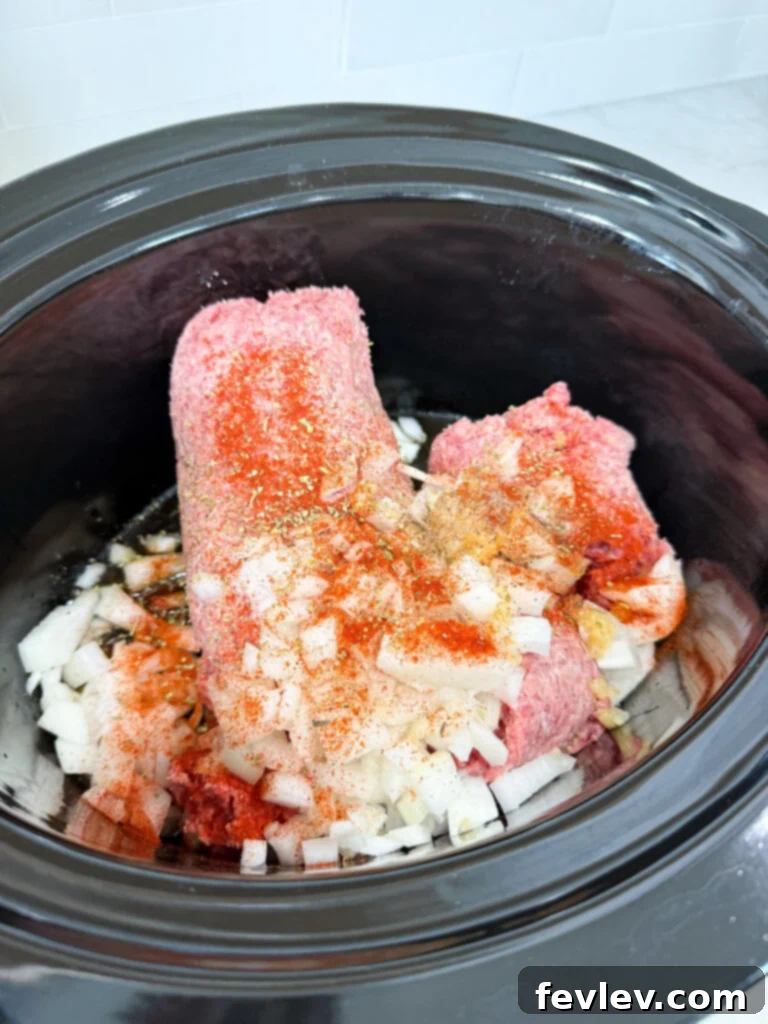Black slow cooker filled with ground beef, onions, and seasoning on a white counter