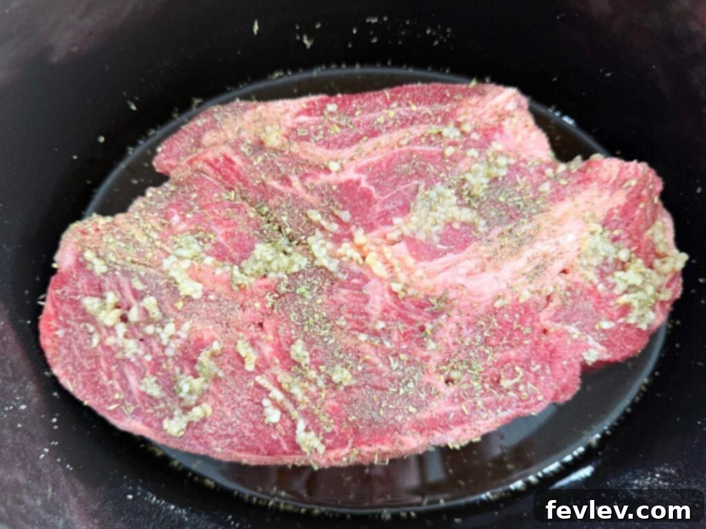 Beef seasoned and cooking in a black slow cooker, becoming tender