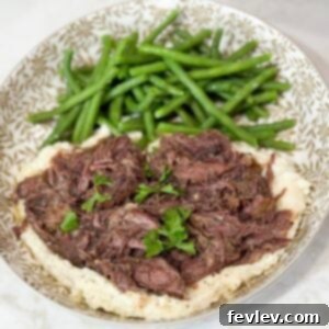Shredded beef over mashed potatoes with green beans on a grey and white plate