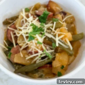 Cooked sausage, potatoes, and green beans in a white bowl topped with parmesan cheese and fresh parsley