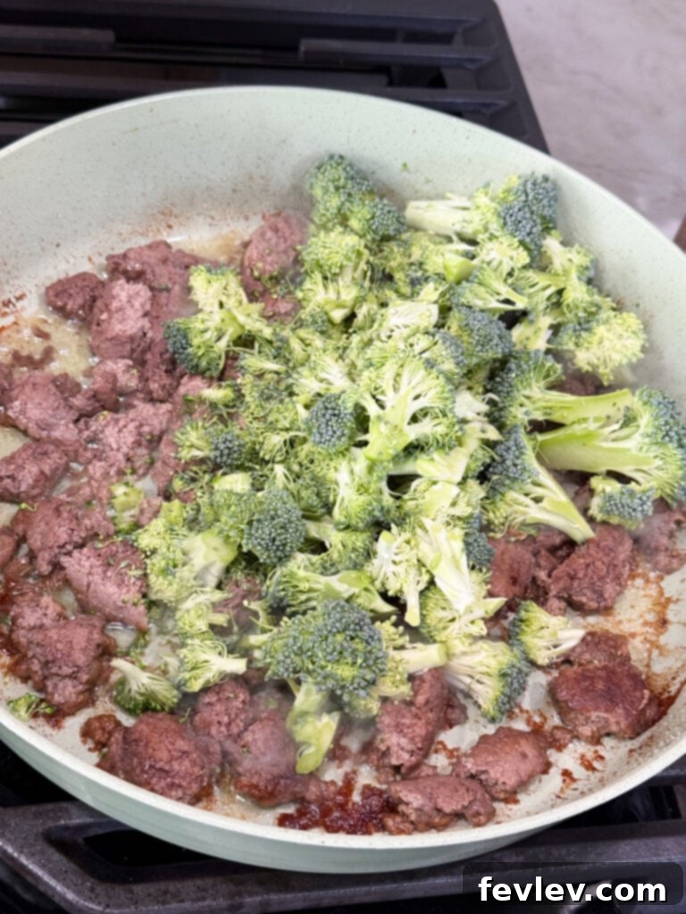 Easy Ground Turkey Hacks 19 A large skillet containing beautifully cooked ground turkey alongside vibrant raw broccoli florets, showcasing the harmonious combination of ingredients for a healthy and balanced meal.