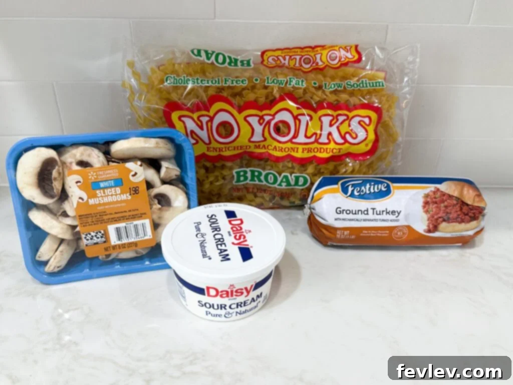 Easy Ground Turkey Hacks 5 A selection of fresh ingredients for a delightful Turkey Stroganoff, including uncooked egg noodles, a package of gourmet mushrooms, creamy sour cream, and lean ground turkey, all neatly displayed on a white kitchen counter.