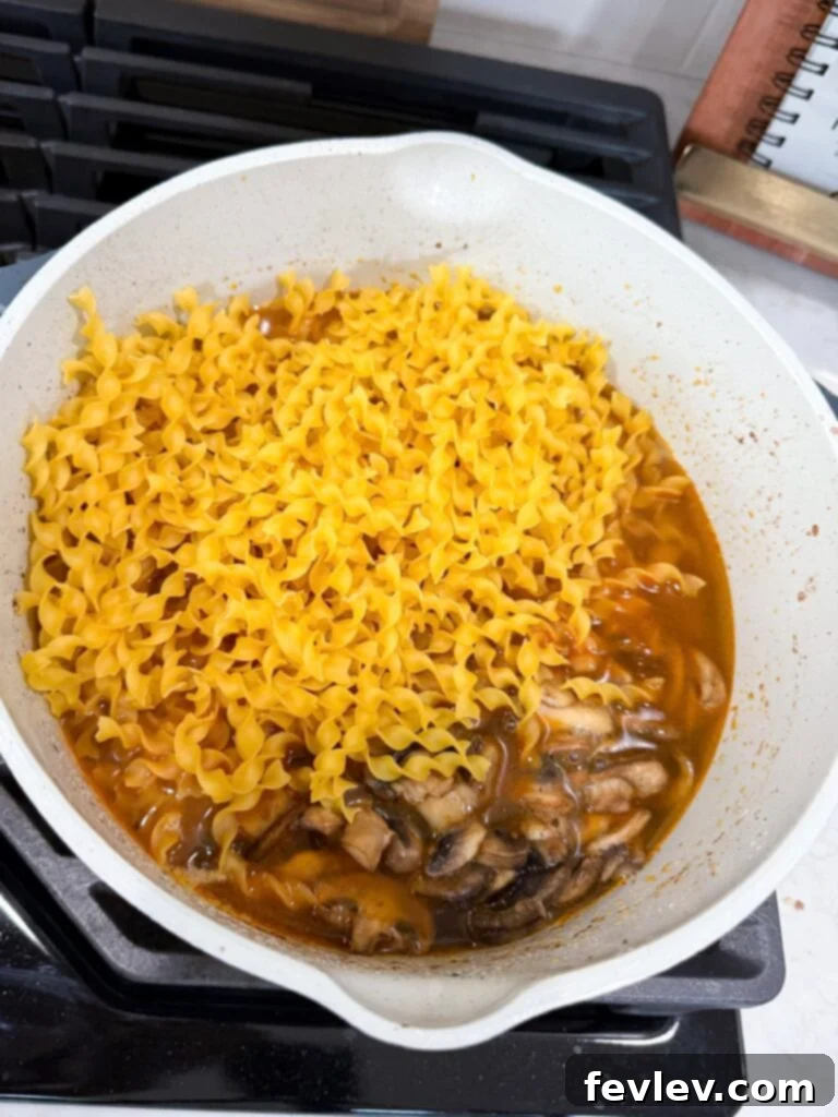 Easy Ground Turkey Hacks 7 A large skillet on the stovetop showing cooked ground turkey simmering in a rich stroganoff sauce, with uncooked egg noodles just added and ready to absorb the flavors, illustrating the simplicity of a one-pan dinner.