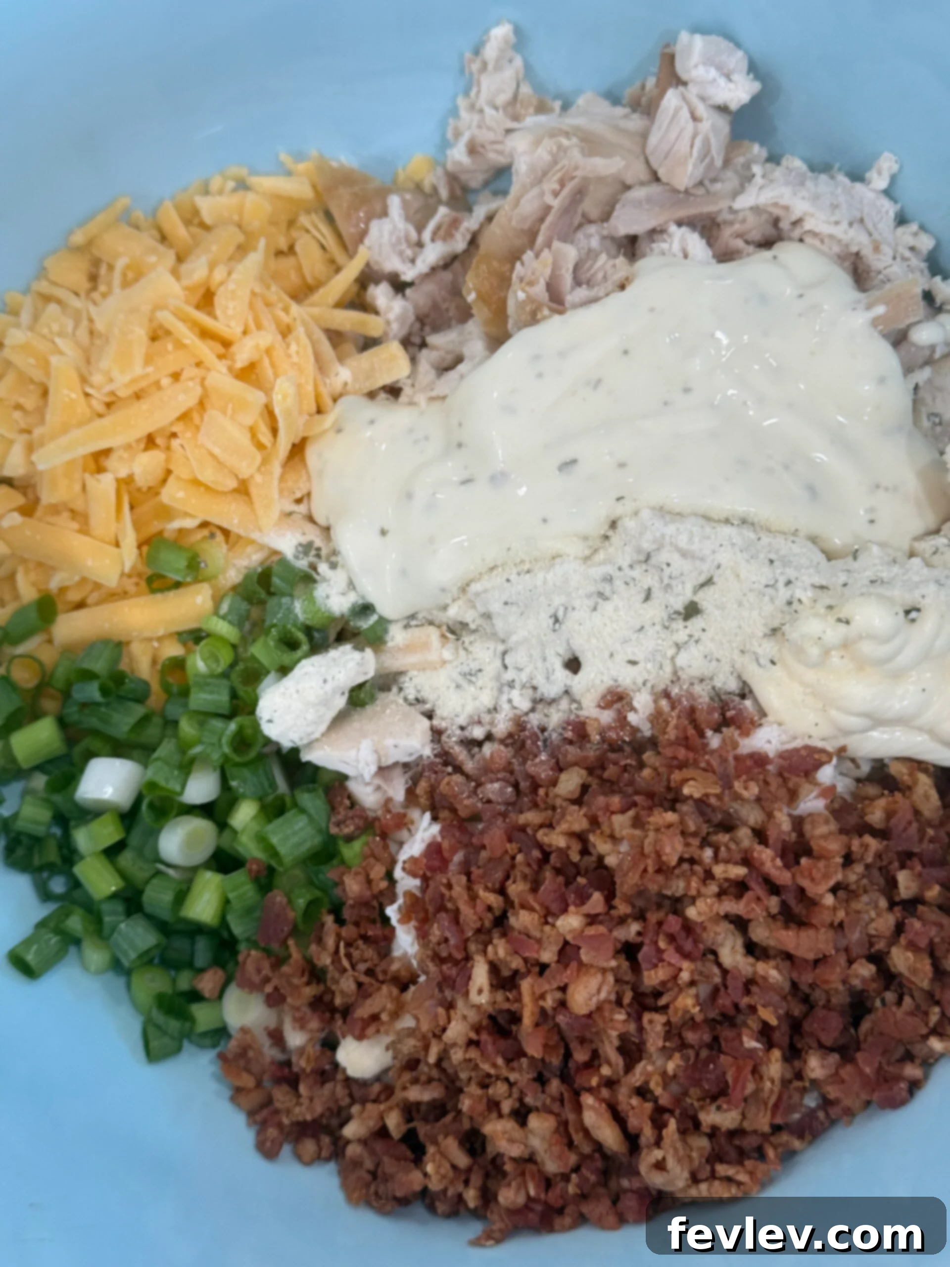 All the ingredients for Bacon Ranch Chicken Salad, including shredded chicken, crispy bacon, ranch dressing, cheese, and green onions, mixed together in a large bowl.