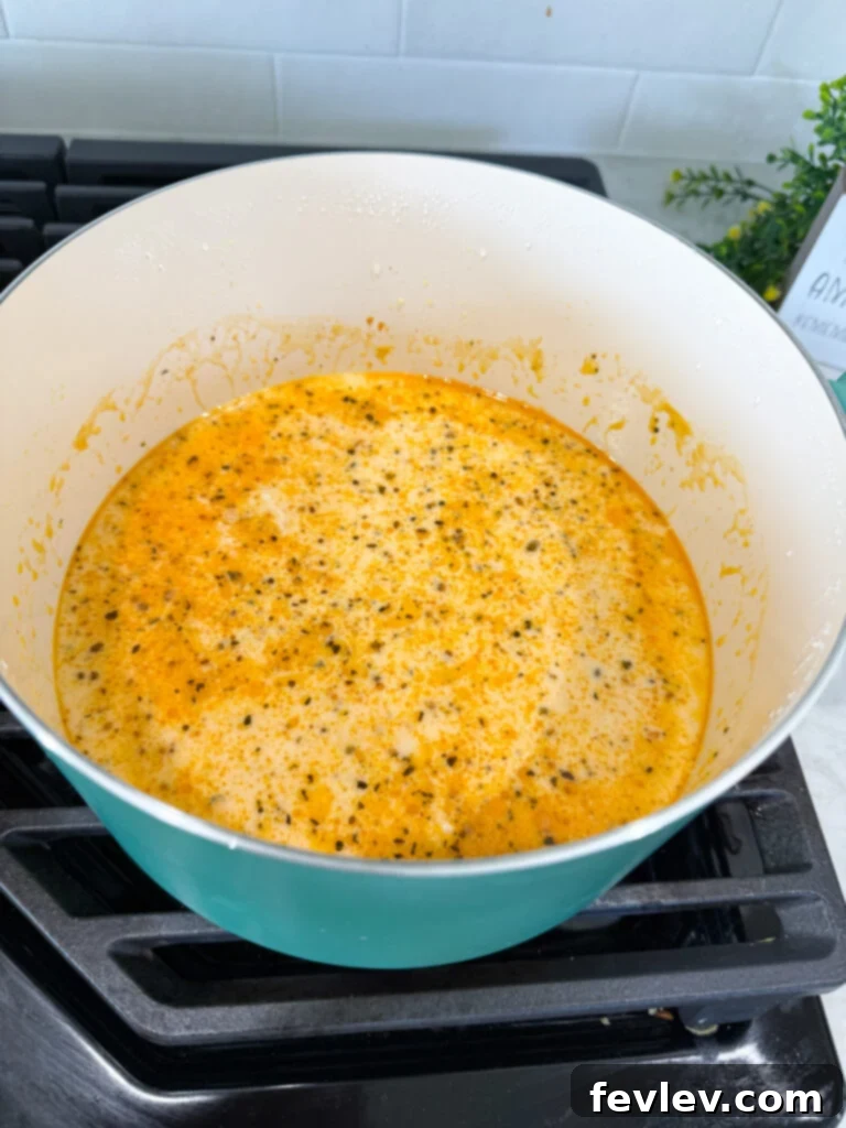 Step 3: Whisking chicken broth into the roux with garlic to create a smooth sauce base.