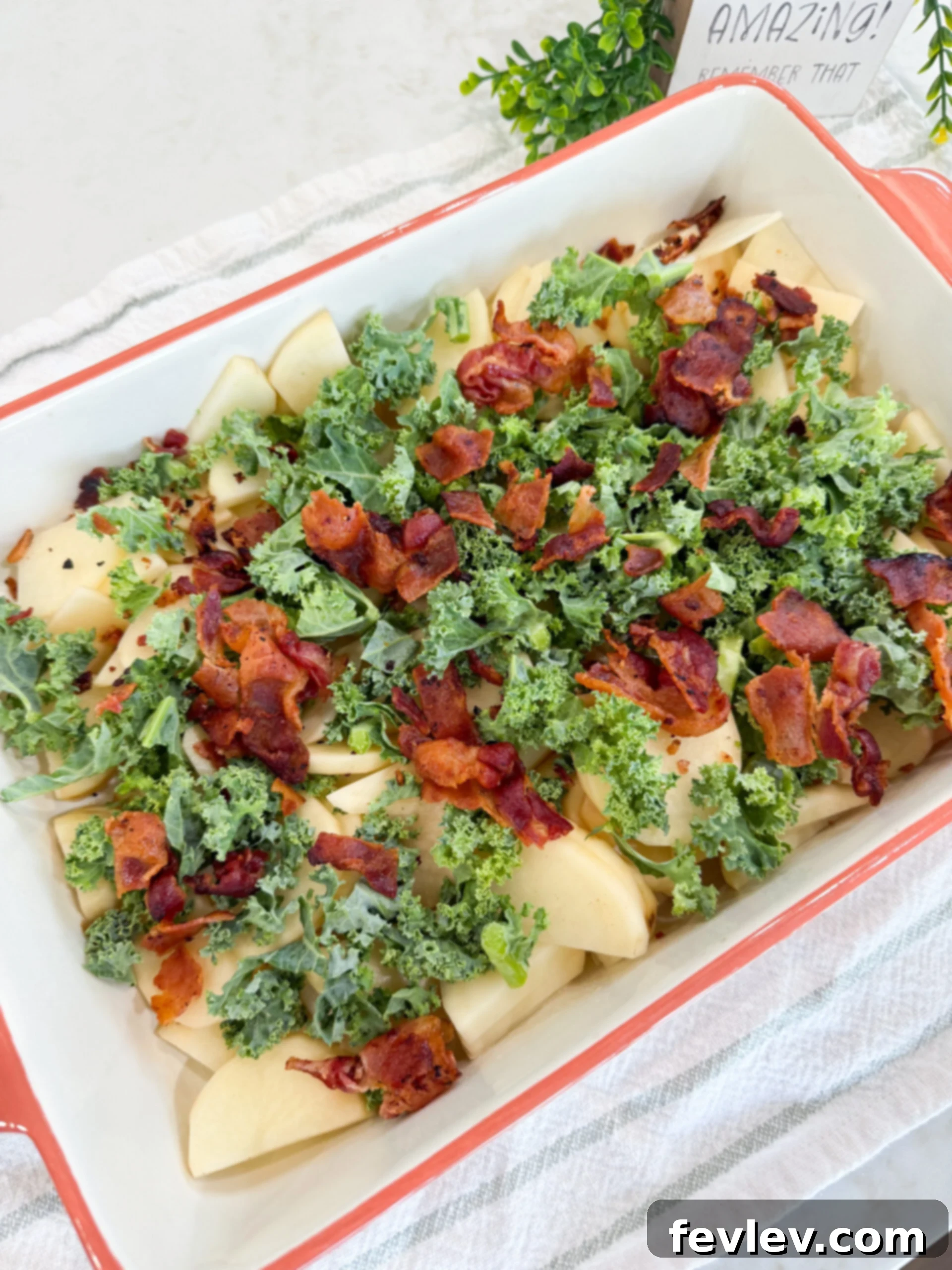 Creamy Tuscan Sausage Potato Kale Casserole 8 Chopped kale and crumbled bacon layered over sliced potatoes in baking dish.