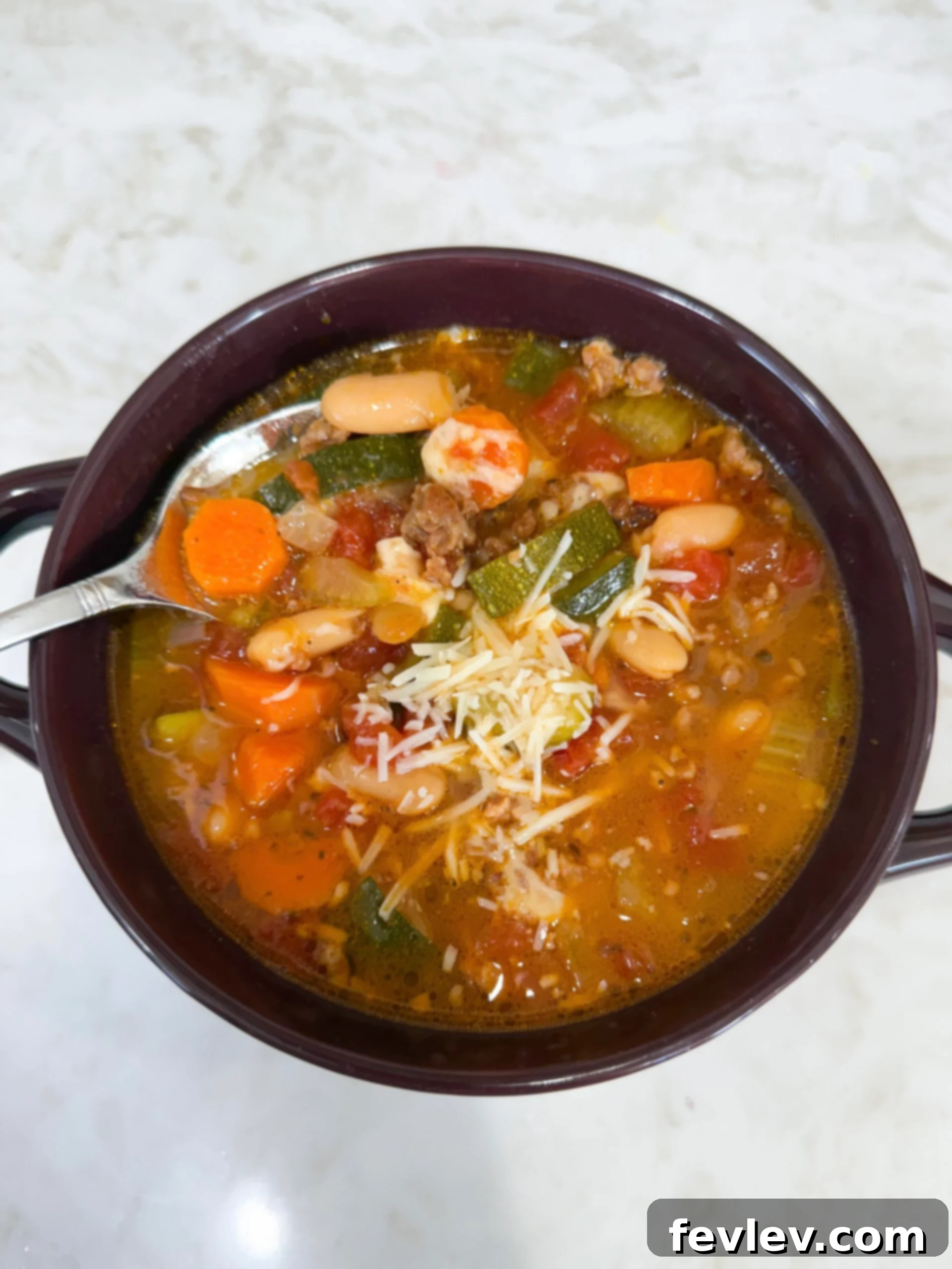 Tuscan Slow Cooker Sausage and Vegetable Soup 2 A steaming bowl of Slow Cooker Italian Vegetable and Sausage Soup, showcasing chunks of savory sausage, vibrant carrots, tender zucchini, and creamy cannellini beans immersed in a rustic, rich tomato broth, garnished with fresh herbs and a sprinkle of Parmesan.