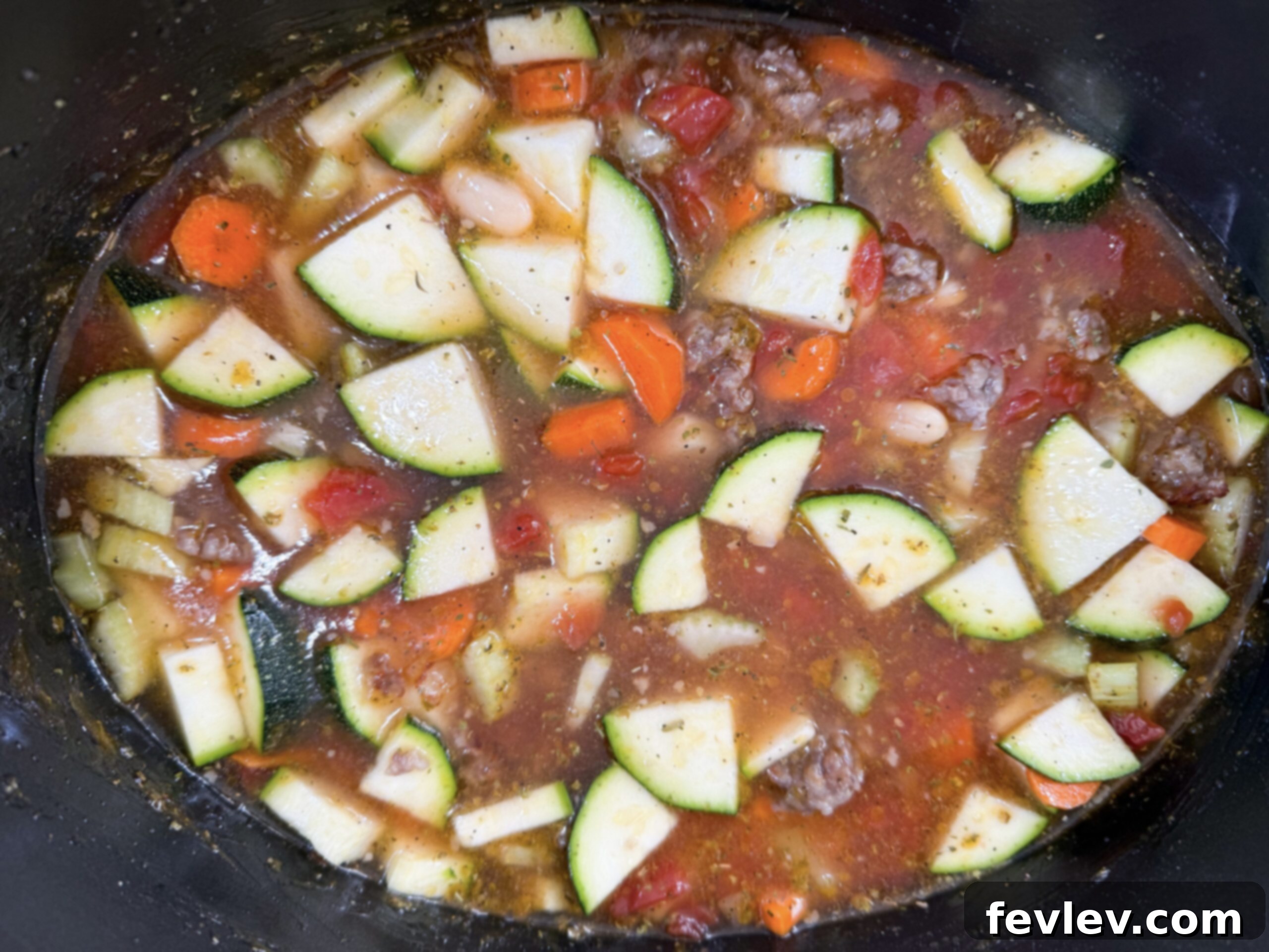 Tuscan Slow Cooker Sausage and Vegetable Soup 5 A top-down view of all the raw ingredients for the Slow Cooker Italian Vegetable and Sausage Soup, including fresh carrots, celery, zucchini, canned diced tomatoes, cannellini beans, chicken broth, and seasonings, neatly arranged in the slow cooker pot before cooking.