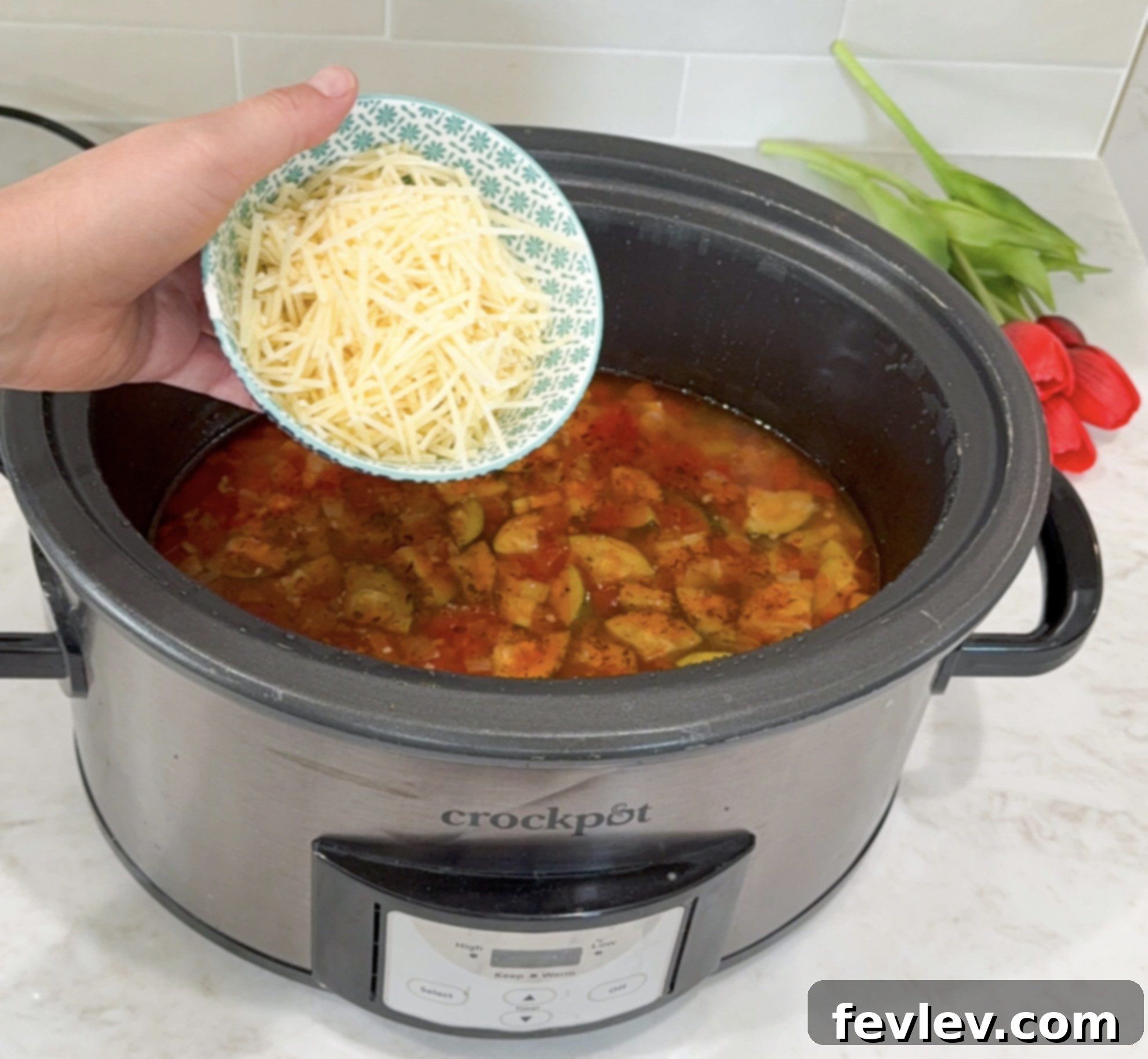 Tuscan Slow Cooker Sausage and Vegetable Soup 7 A hand stirring a generous amount of grated Parmesan cheese into the hot Slow Cooker Italian Vegetable and Sausage Soup, illustrating the final step to achieve a creamy, rich texture before serving.