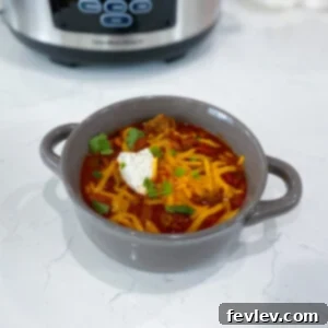 A hearty bowl of Slow Cooker Chili, topped with shredded cheese and a dollop of sour cream, ready to be devoured.
