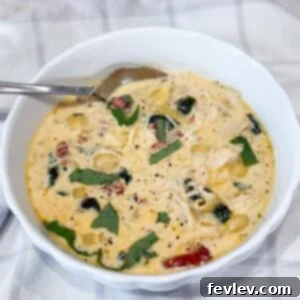 A steaming bowl of creamy Slow Cooker Marry Me Chicken Soup, garnished with pasta, fresh spinach, and sun-dried tomatoes, ready to be enjoyed.