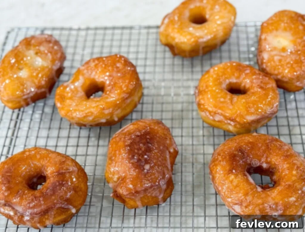 A batch of golden, freshly made glazed donuts, artfully arranged on a cooling rack, made from simple biscuit dough.