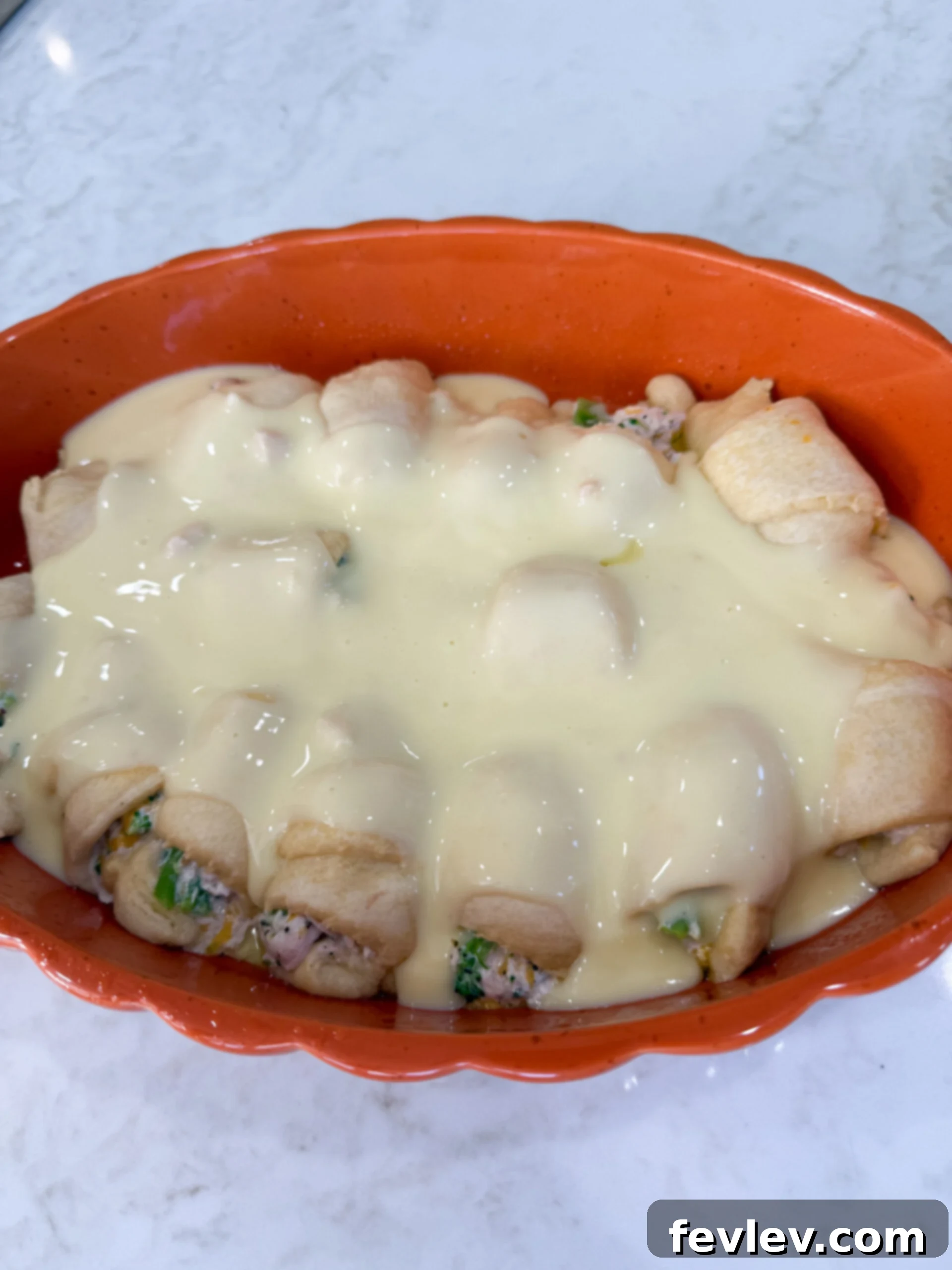Pouring creamy sauce over crescent rolls in baking dish
