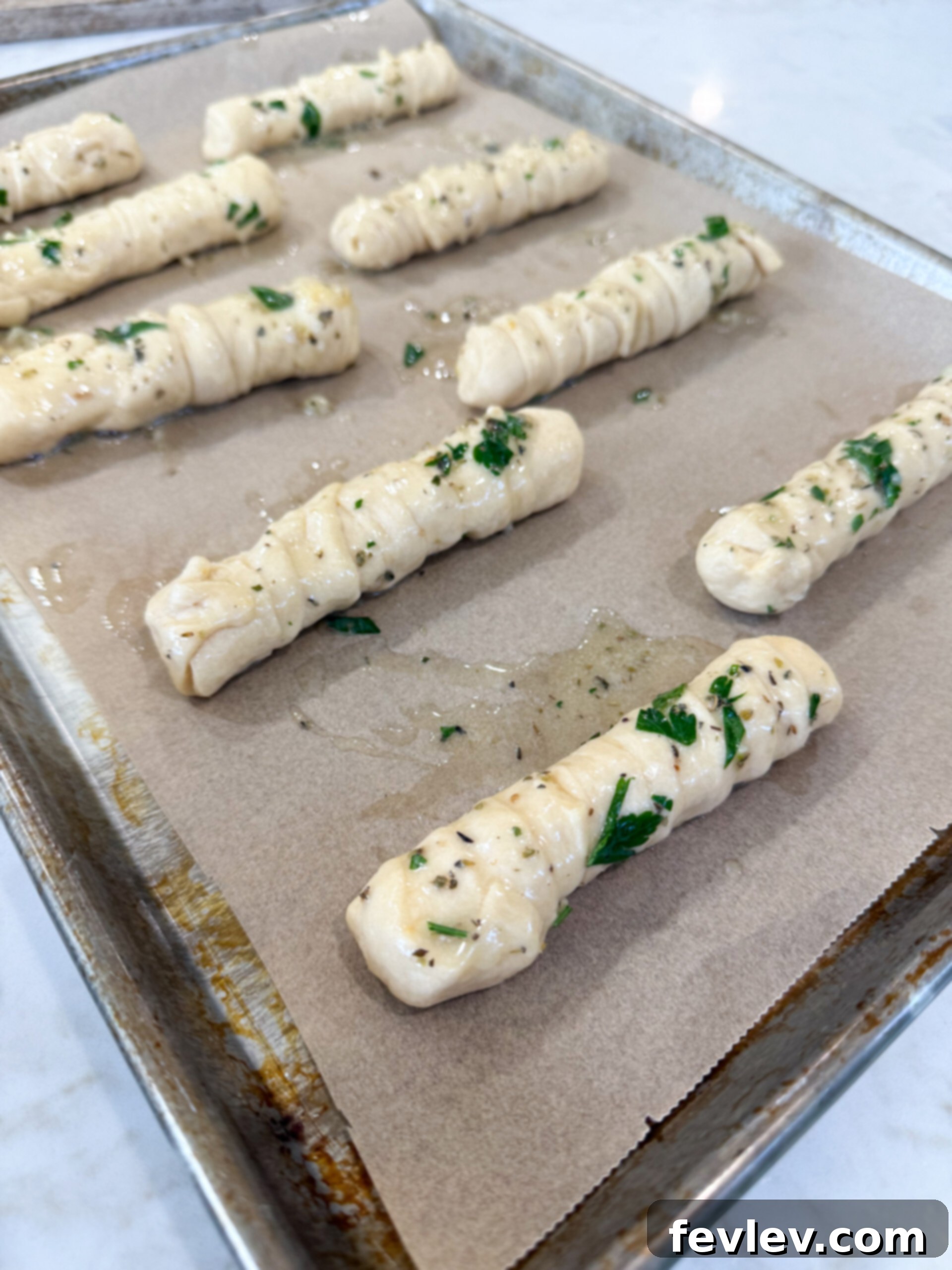Applying garlic butter generously over the wrapped mozzarella-stuffed breadsticks on a baking sheet.