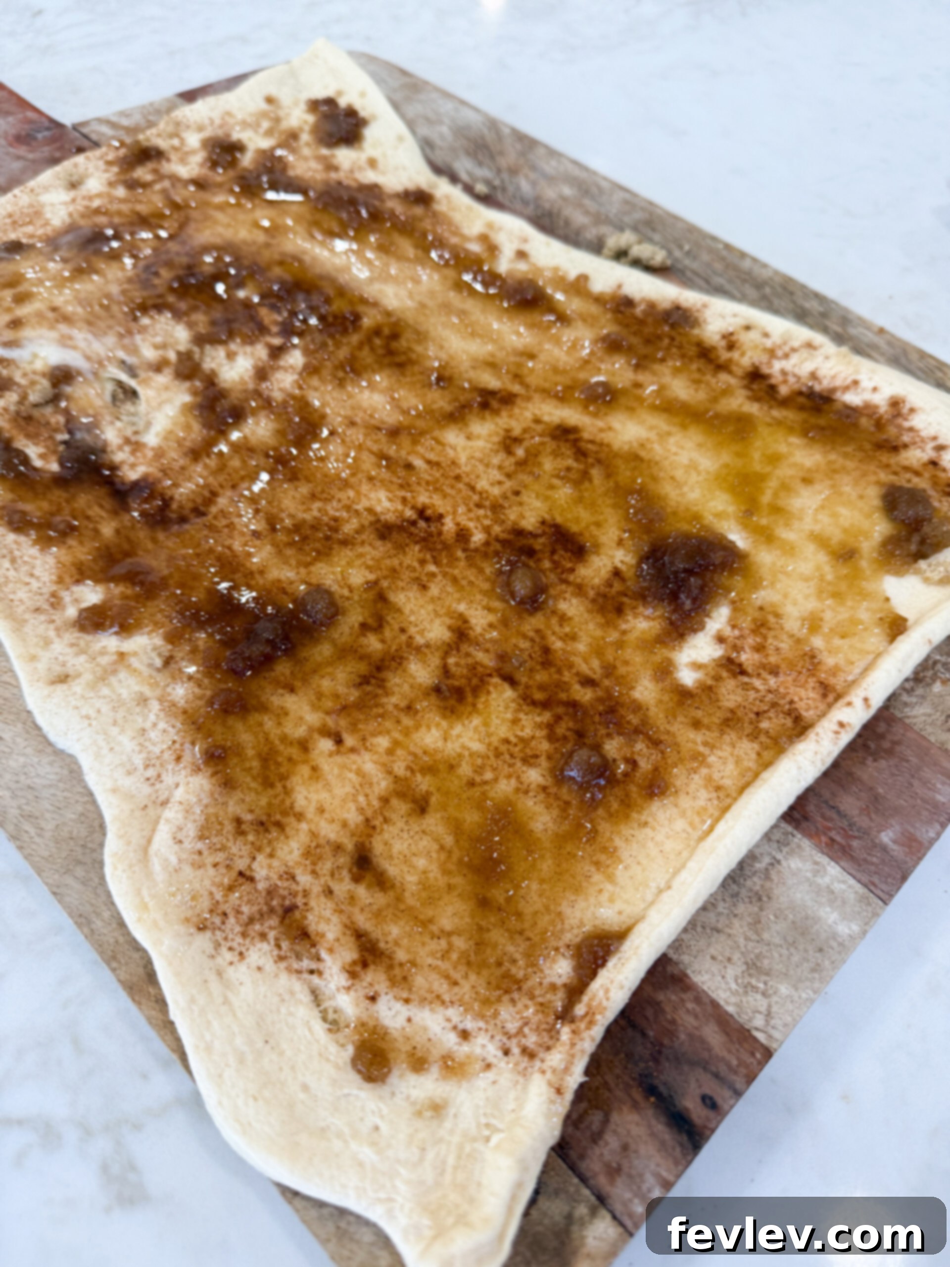 A hand sprinkling cinnamon sugar mixture evenly over buttered crescent dough.