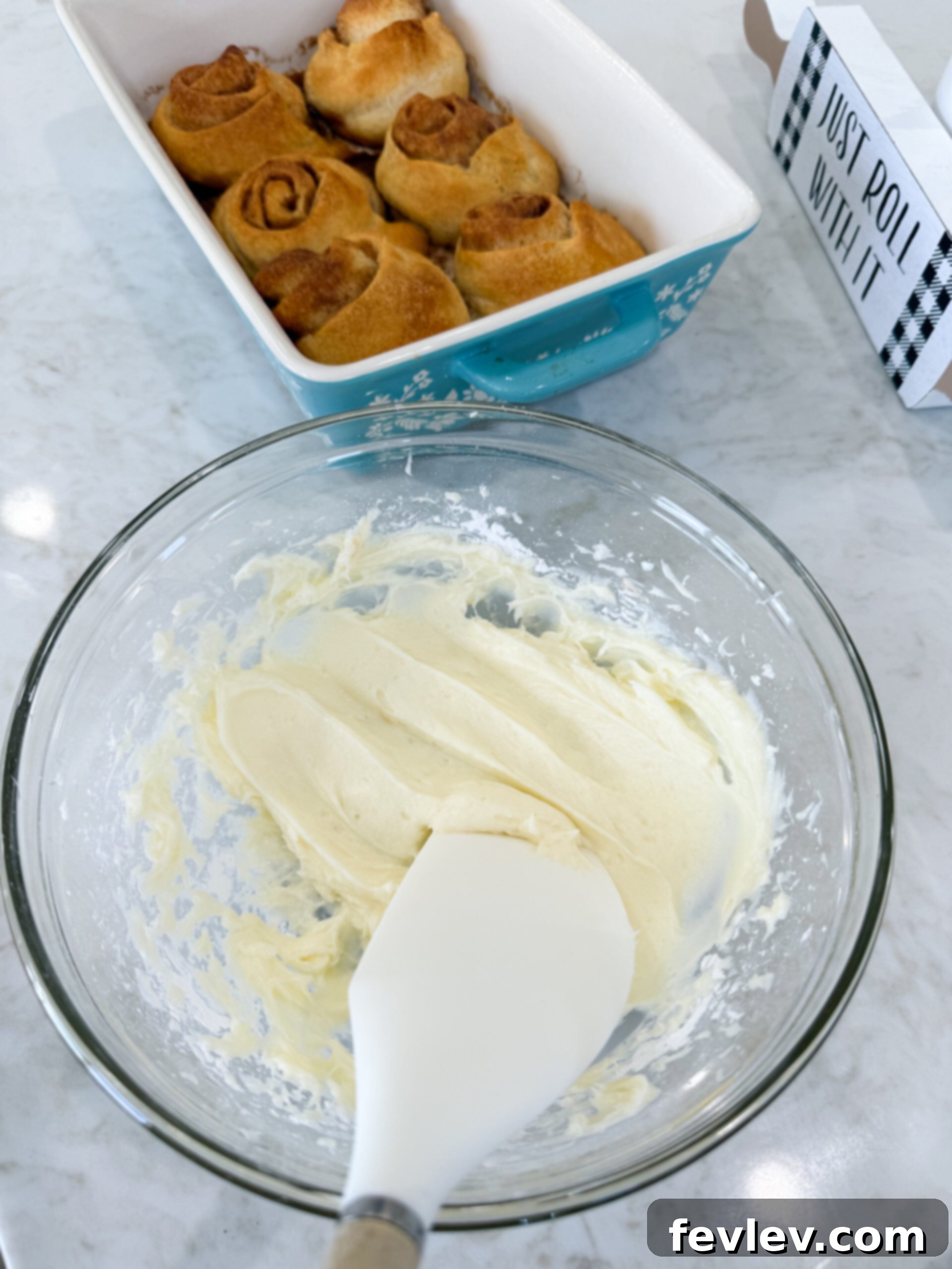Cream cheese frosting being mixed to a smooth consistency in a glass mixing bowl.