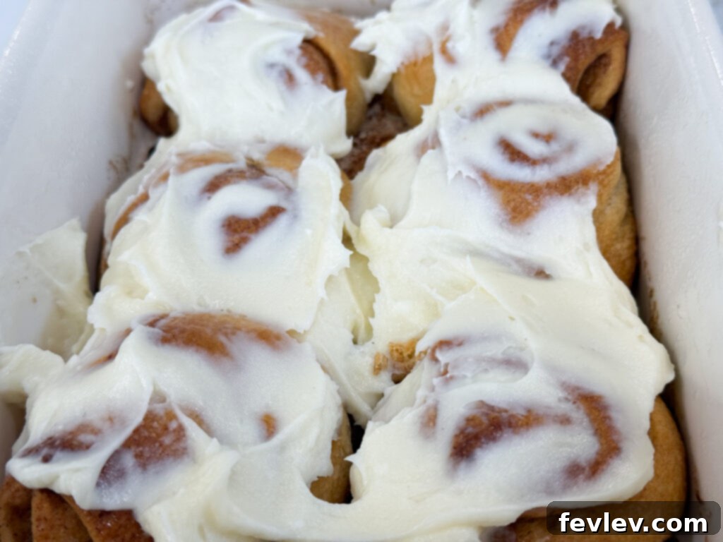 Freshly baked crescent roll cinnamon rolls topped with melted cream cheese frosting in a square pan.