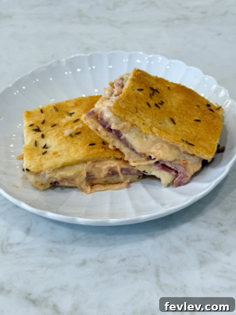 Pastrami Crescent Melt 2 Golden-brown Pastrami Crescent Sandwich Bake, sliced into squares, with flaky crust and visible layers of pastrami, Swiss cheese, and sauerkraut.