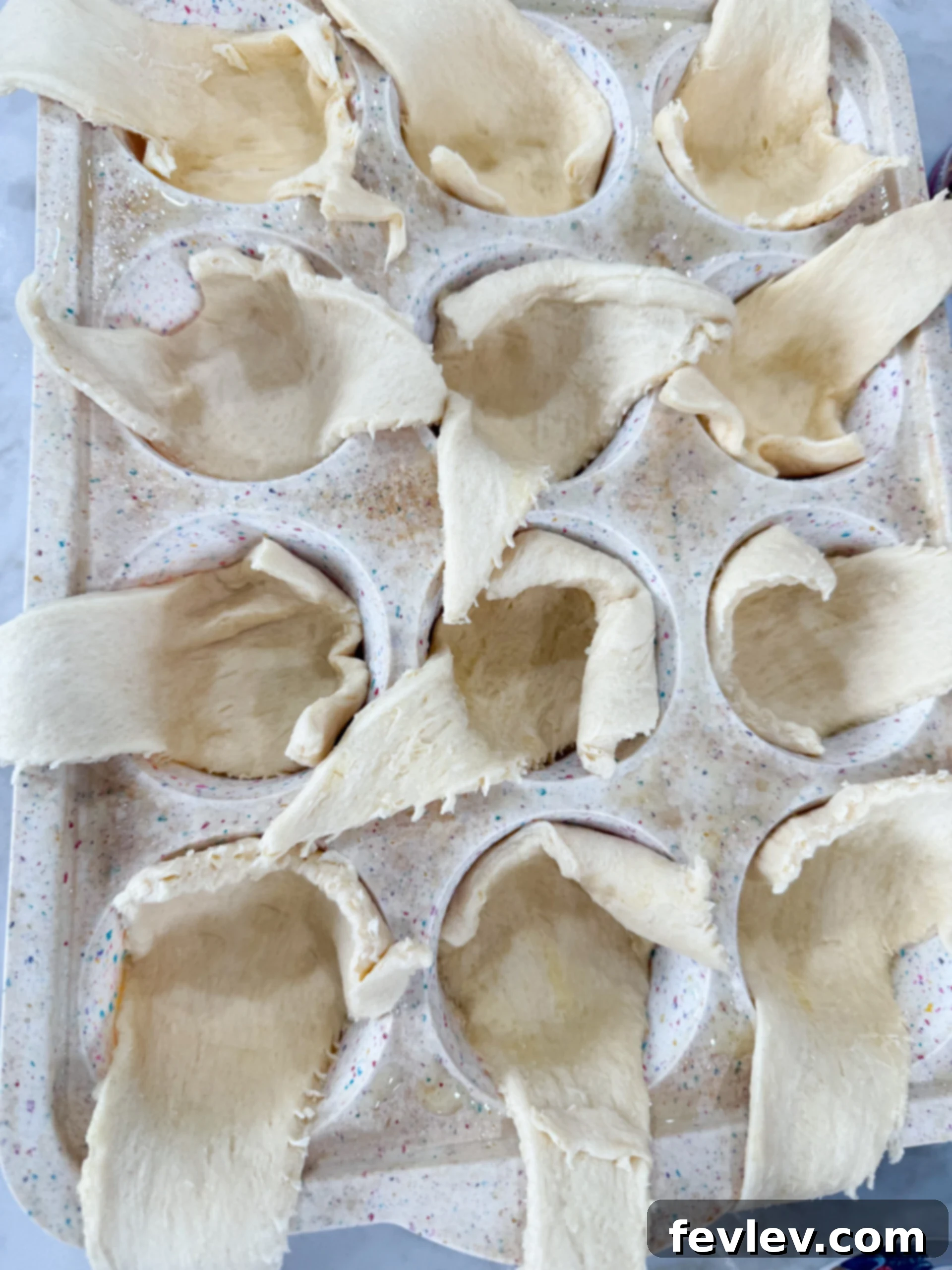 Carefully pressing crescent dough triangles into muffin tin cups, preparing the base for mini cheesecake pies.
