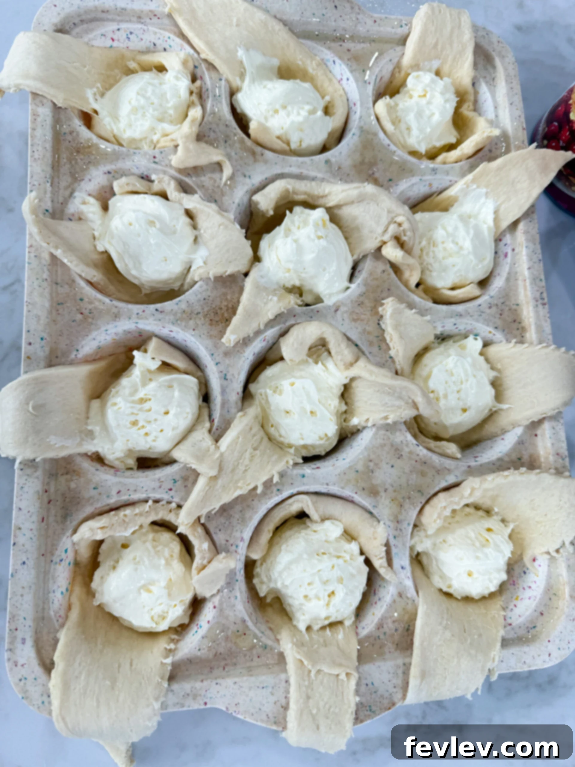 Spoonfuls of creamy cheesecake filling being added into crescent dough-lined muffin cups, forming the sweet core.