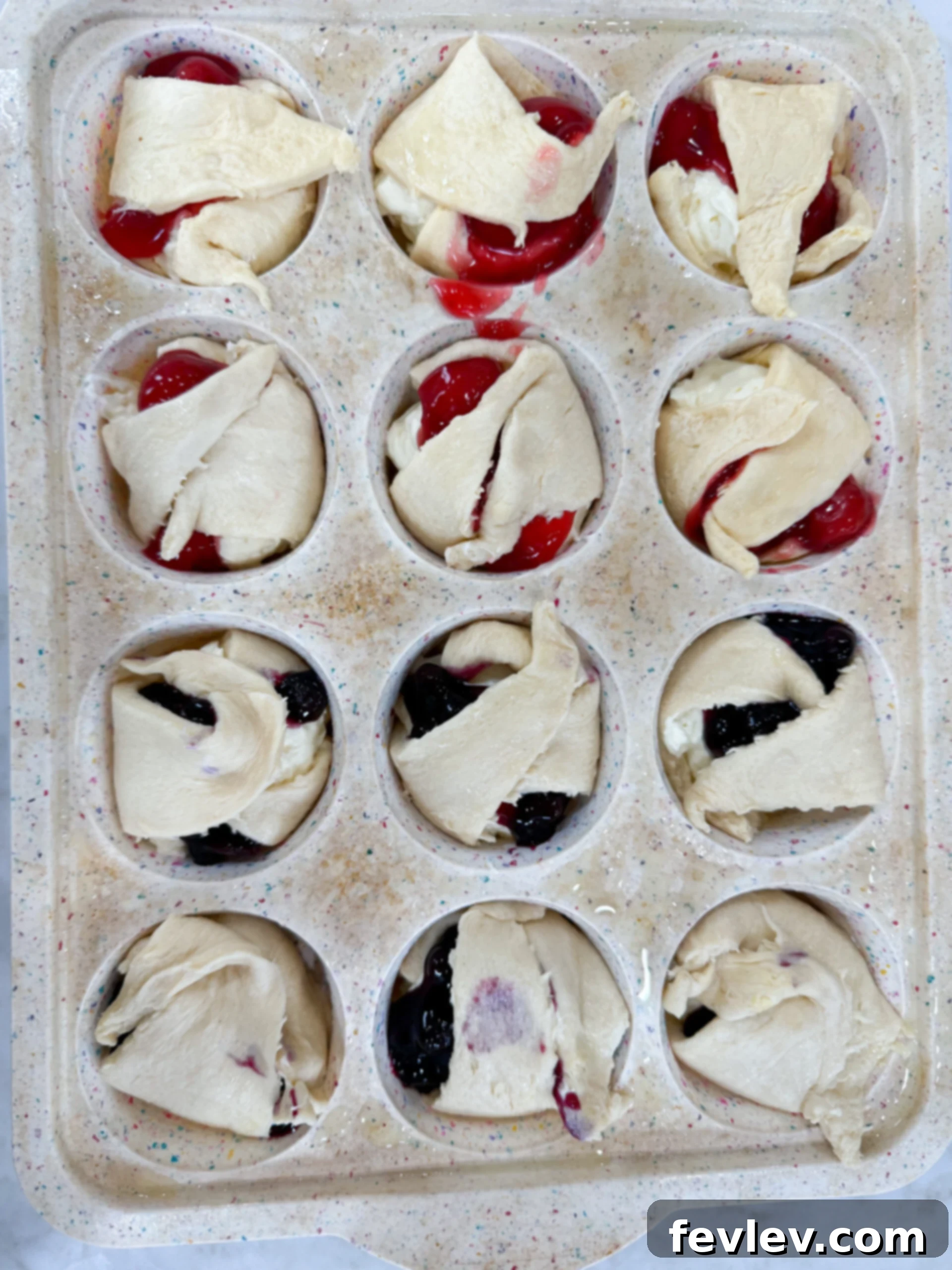 The edges of crescent dough gently folded inwards over the fruit and cheesecake filling in muffin cups, creating a rustic look.