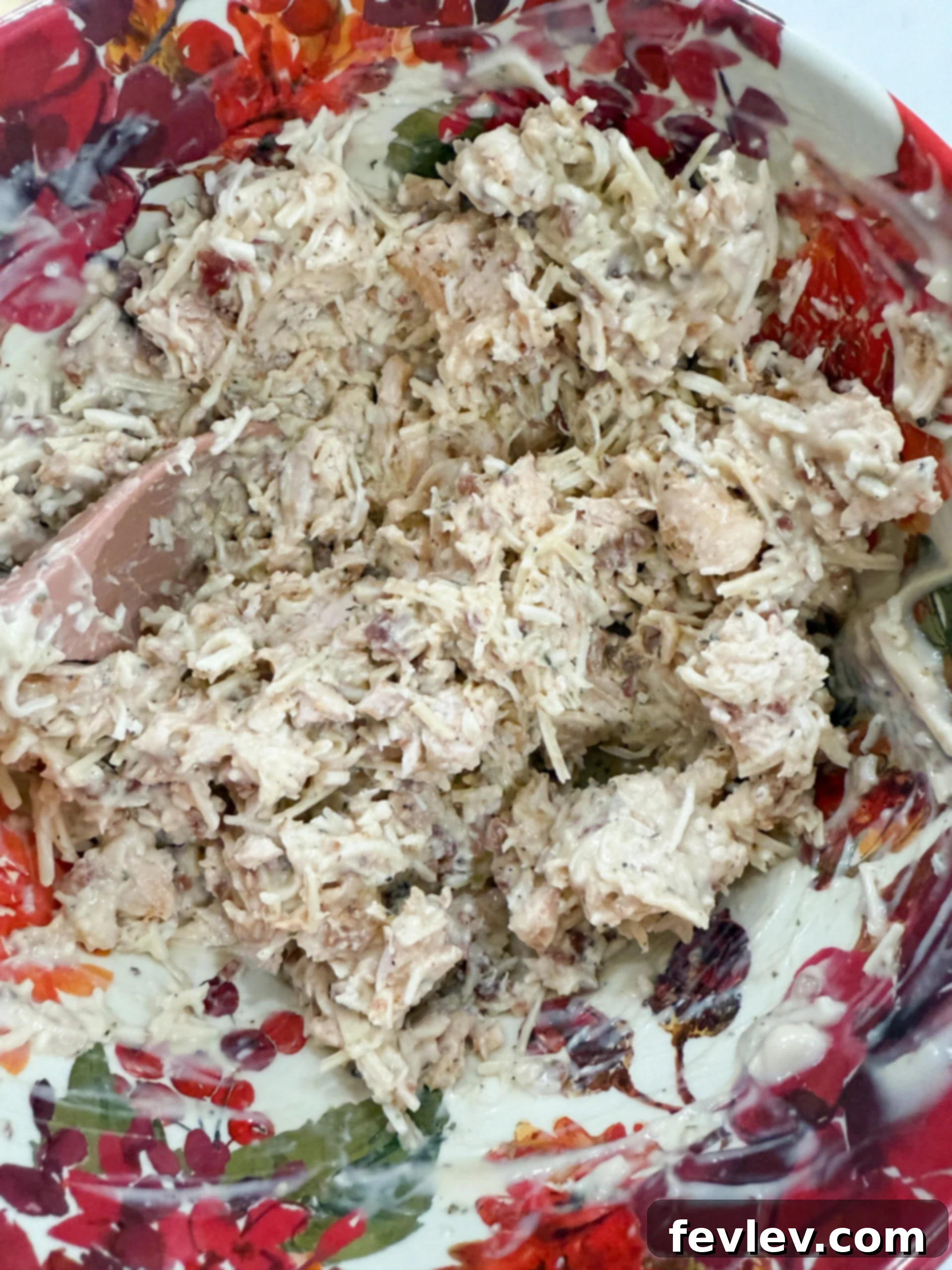 Golden Bacon Alfredo Bake 5 A large mixing bowl containing shredded chicken, creamy Alfredo sauce, crispy bacon pieces, a medley of seasonings, and both Parmesan and mozzarella cheeses, perfectly combined.