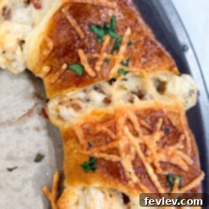 Golden baked crescent ring stuffed with chicken, bacon, and Alfredo sauce, presented on a round cutting board.