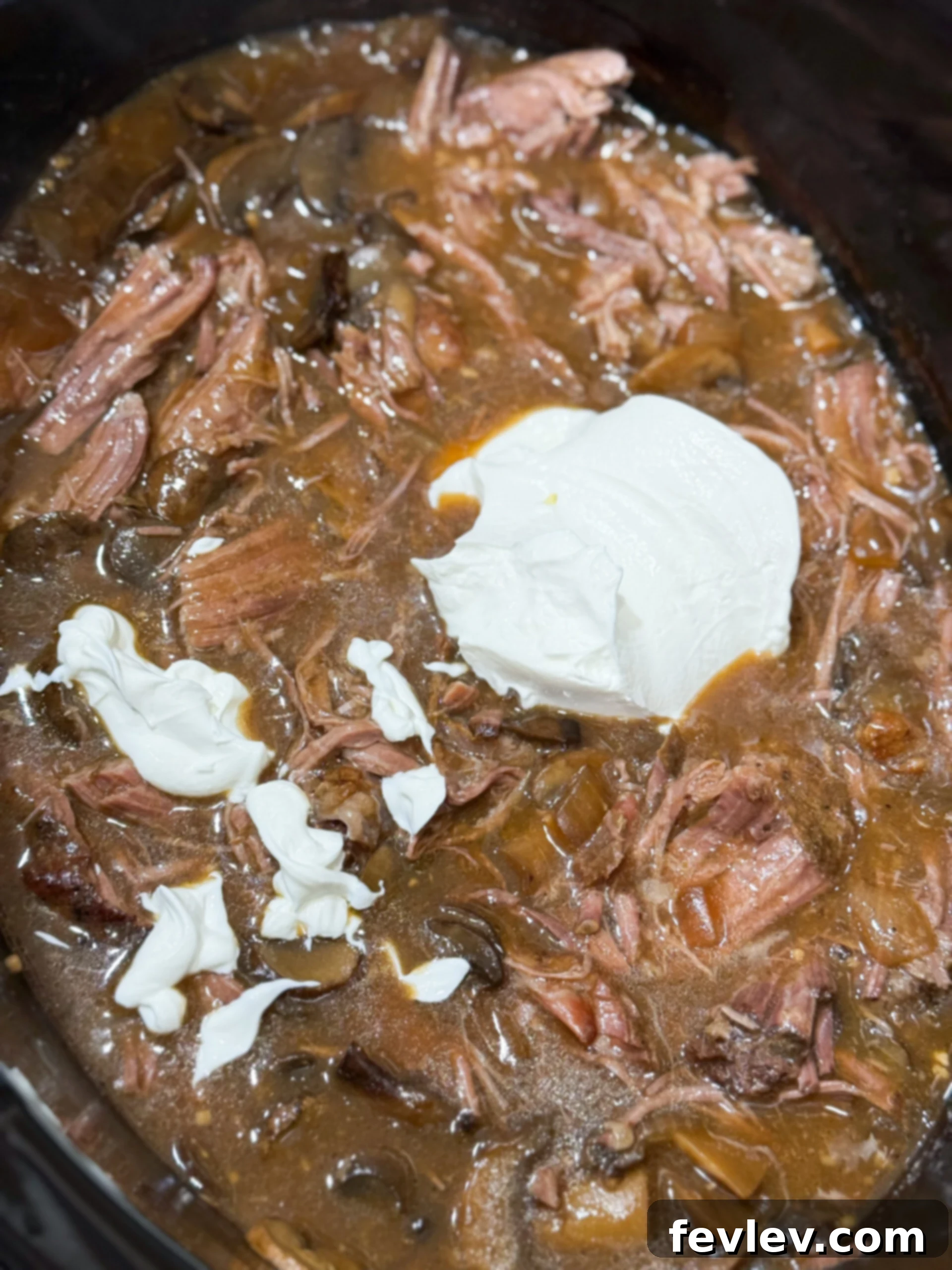 Tender & Creamy Slow Cooker Beef Stroganoff 10 Sour cream being stirred into the finished beef stroganoff in the slow cooker, creating a creamy texture