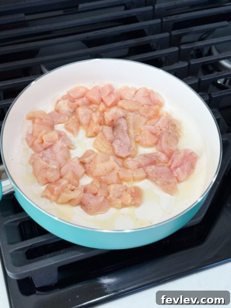 Cubed chicken breast searing in a hot skillet with olive oil, seasoned with salt and pepper, achieving a golden-brown crust.
