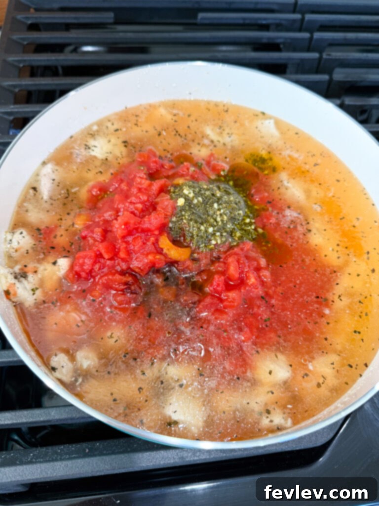 Chicken broth, diced tomatoes, vibrant basil pesto, and balsamic vinegar simmering together in a skillet, creating a rich and aromatic sauce base for the Caprese Chicken and Rice.