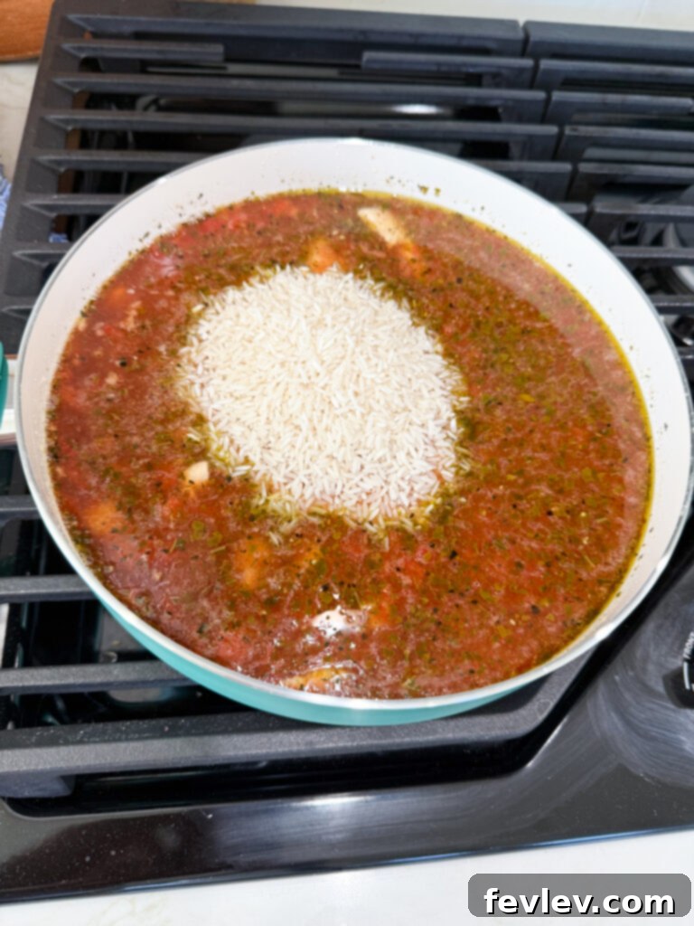 White rice and cooked chicken simmering in the vibrant Caprese sauce, covered, allowing the rice to absorb all the delicious liquid and cook through to a tender consistency.