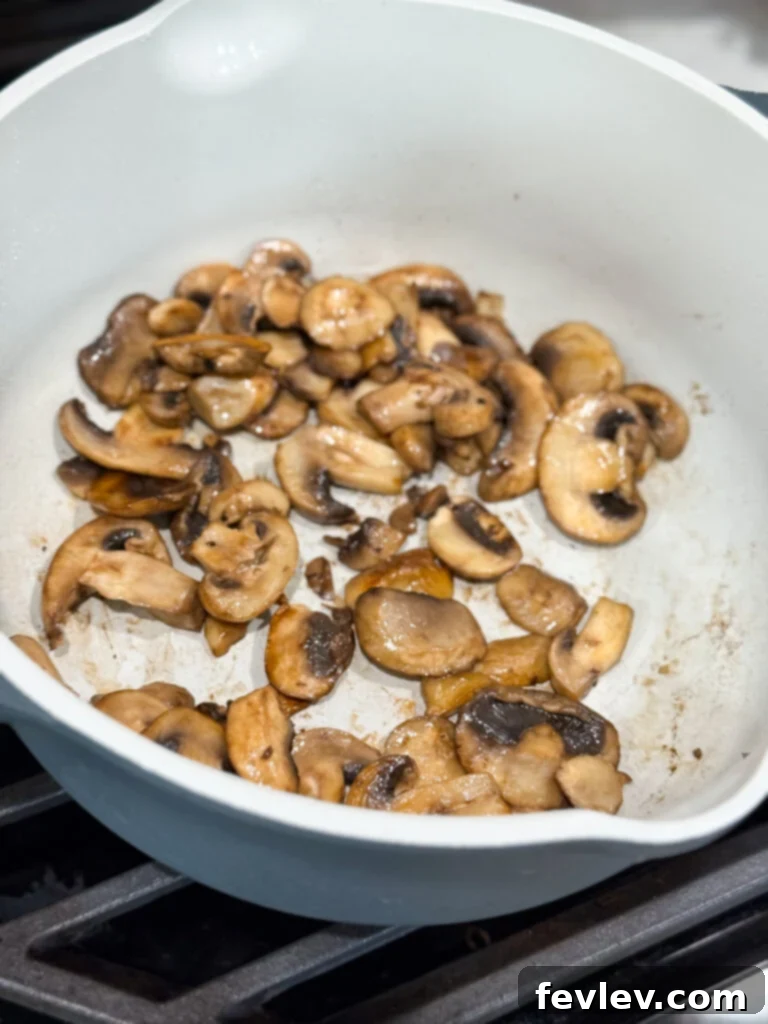 Beef Stroganoff 5 Sliced mushrooms being sautéed until golden brown in a large skillet, developing deep flavor before being removed to a plate.