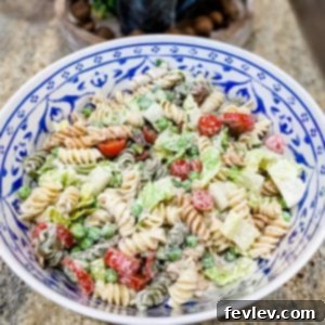Vibrant and fresh Summer Pasta Salad with rotini noodles, green peas, halved cherry tomatoes, and crispy bacon bits, garnished with sliced green onions in a large white serving bowl.