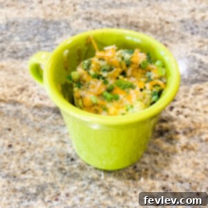Delicious and fluffy microwave loaded omelette in a mug, garnished with fresh green onions and cheese.