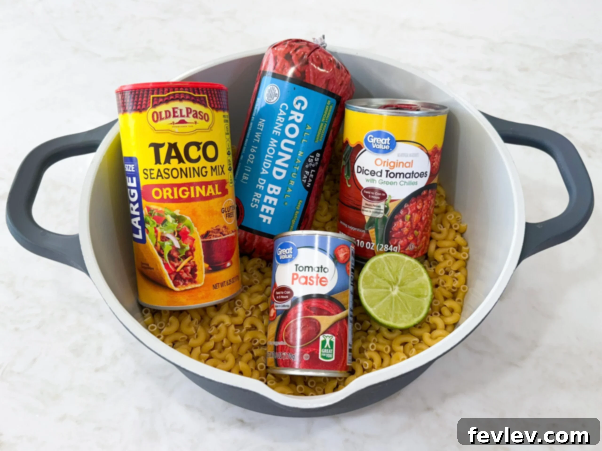 All the fresh and pantry staple ingredients for Easy Taco Pasta One Pot Skillet Dinner laid out neatly next to a cooking pot.