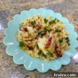 Creamy Slow Cooker Tuscan Chicken served over pasta, garnished with fresh herbs and a sprinkle of Parmesan cheese.