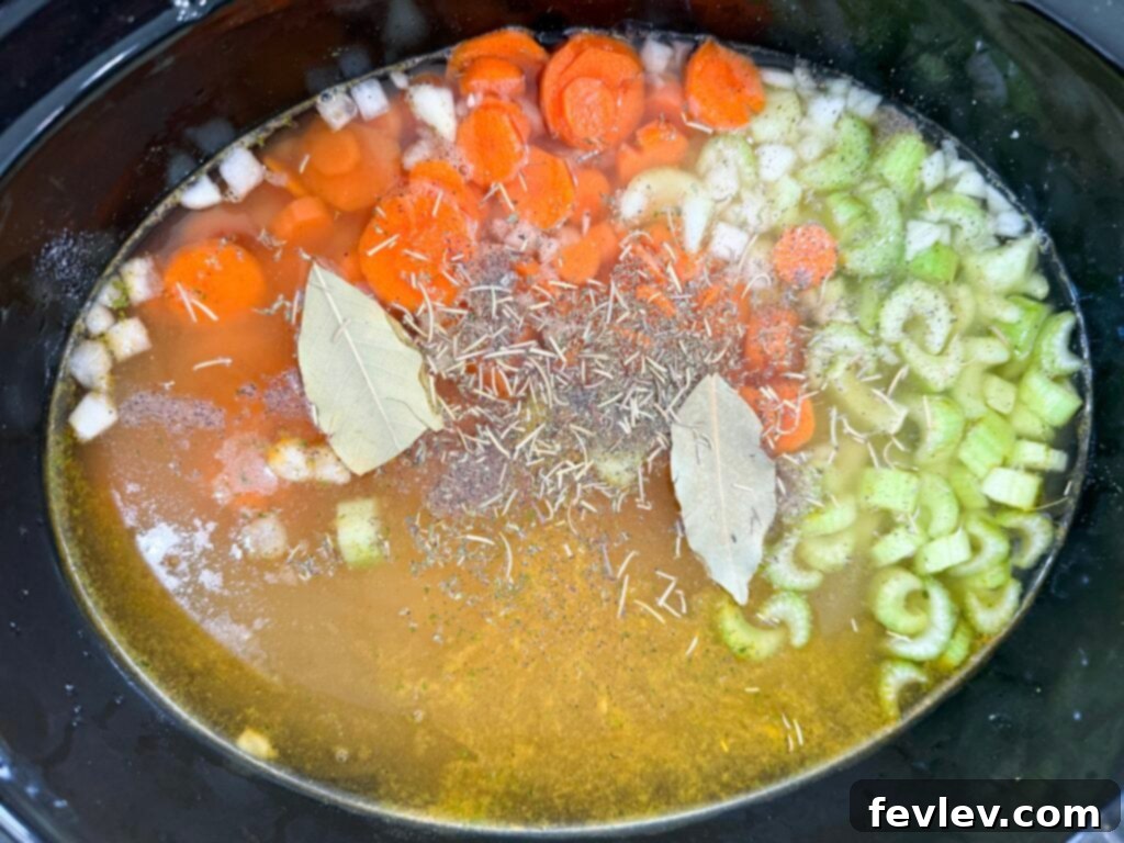 Raw vegetables and chicken breasts submerged in broth within a slow cooker, ready for cooking.
