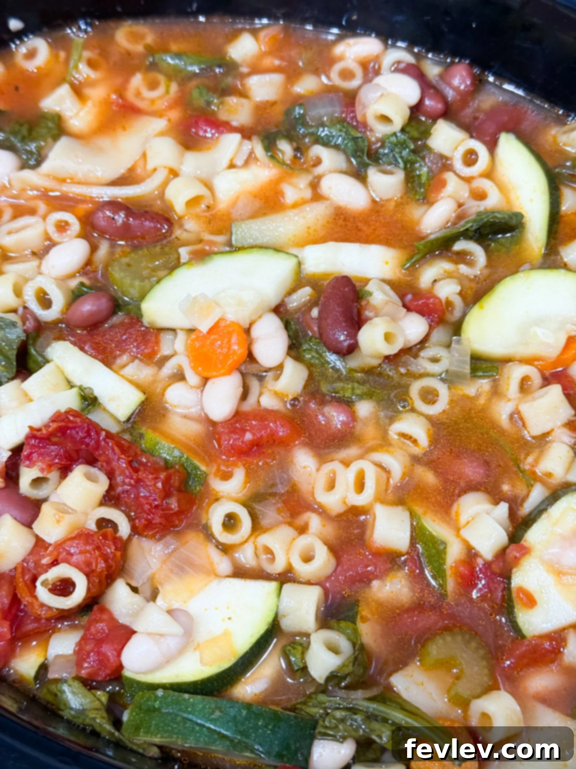 Minestrone soup simmering in a slow cooker, with all vegetables and pasta perfectly cooked and integrated.