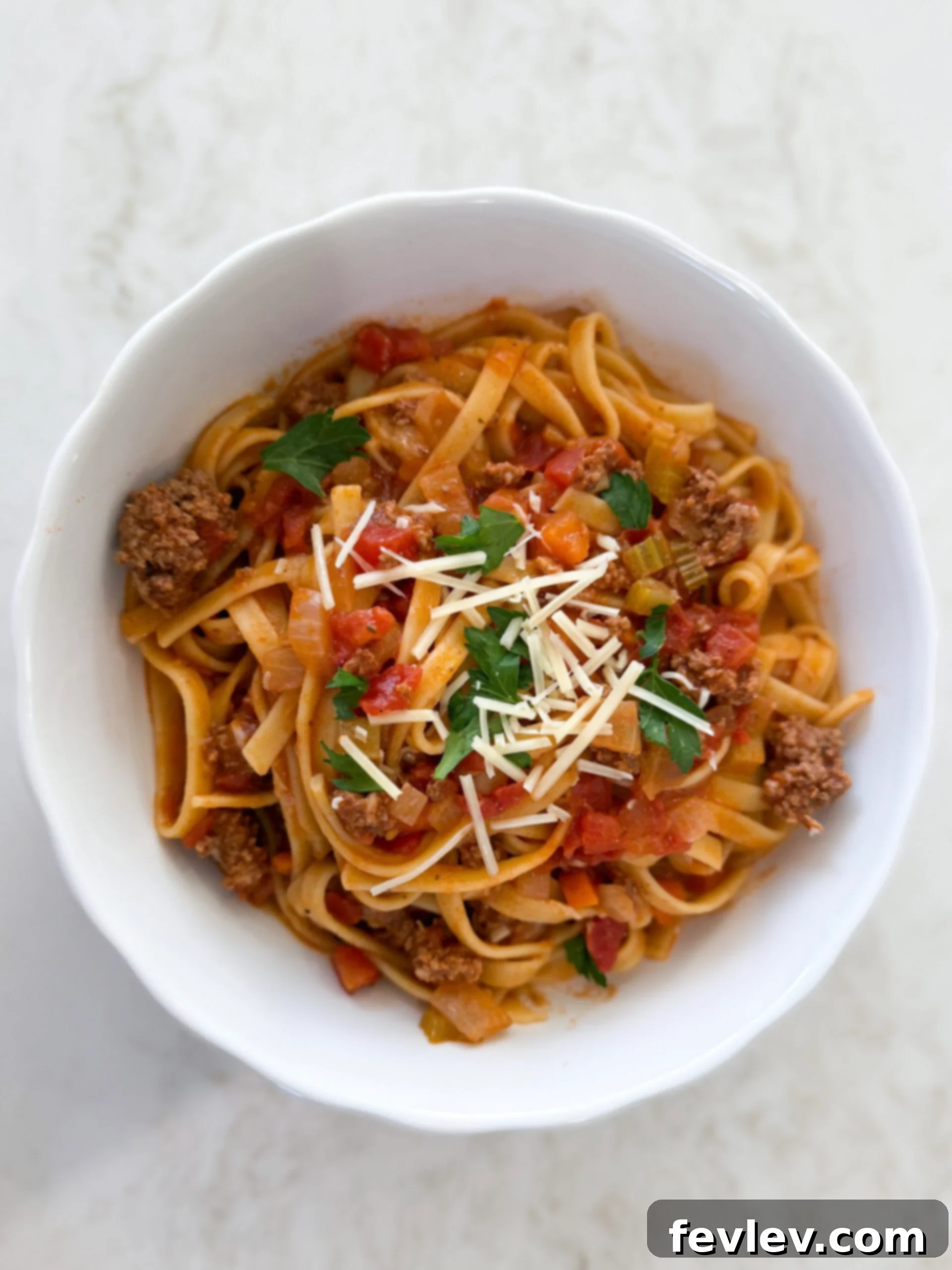 A beautifully plated One-Pot Beef Bolognese with fresh pasta, garnished with grated Parmesan cheese and a sprig of basil.