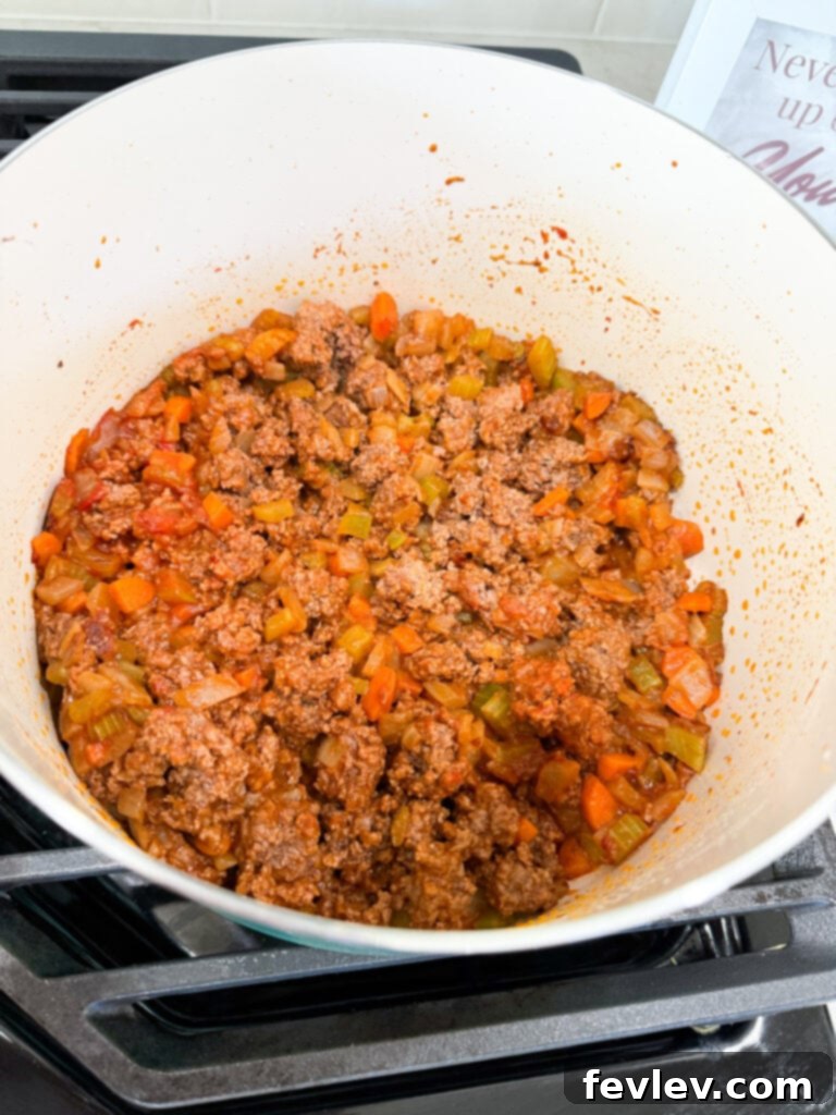 Ground beef browning in a Dutch oven with sautéed vegetables and tomato paste, preparing for the sauce.