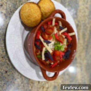 A vibrant bowl of Chicken Taco Soup garnished with fresh cilantro, sour cream, and crispy tortilla strips, served with a side of lime wedges.